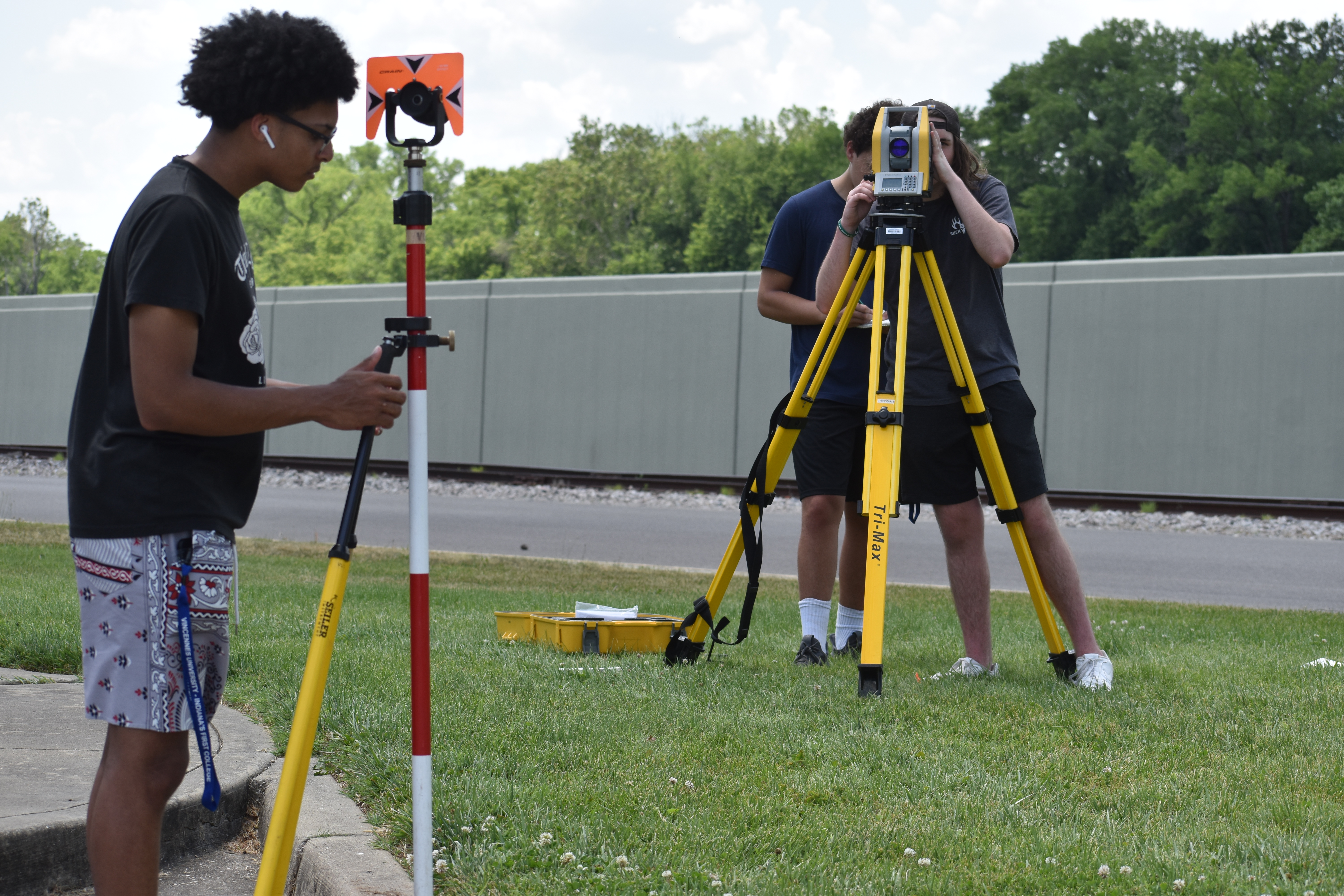 Three male students using surveying equipment outdoors.